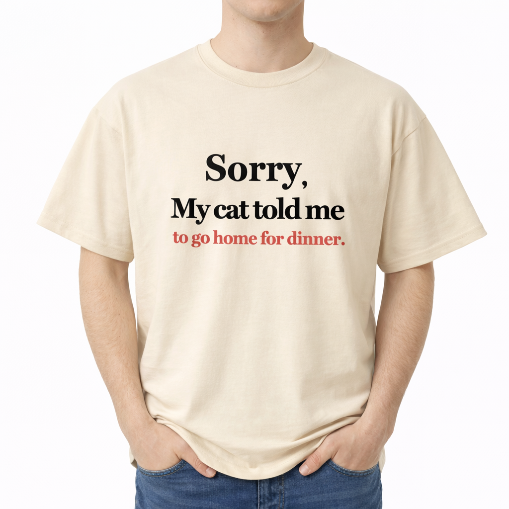 Person wearing a beige t-shirt with humorous text about a cat telling the wearer to go home for dinner. The center chest features the phrase "Sorry, My cat told me to go home for dinner." printed in a classic serif font. The first two lines of text are black, and the bottom line is red.
