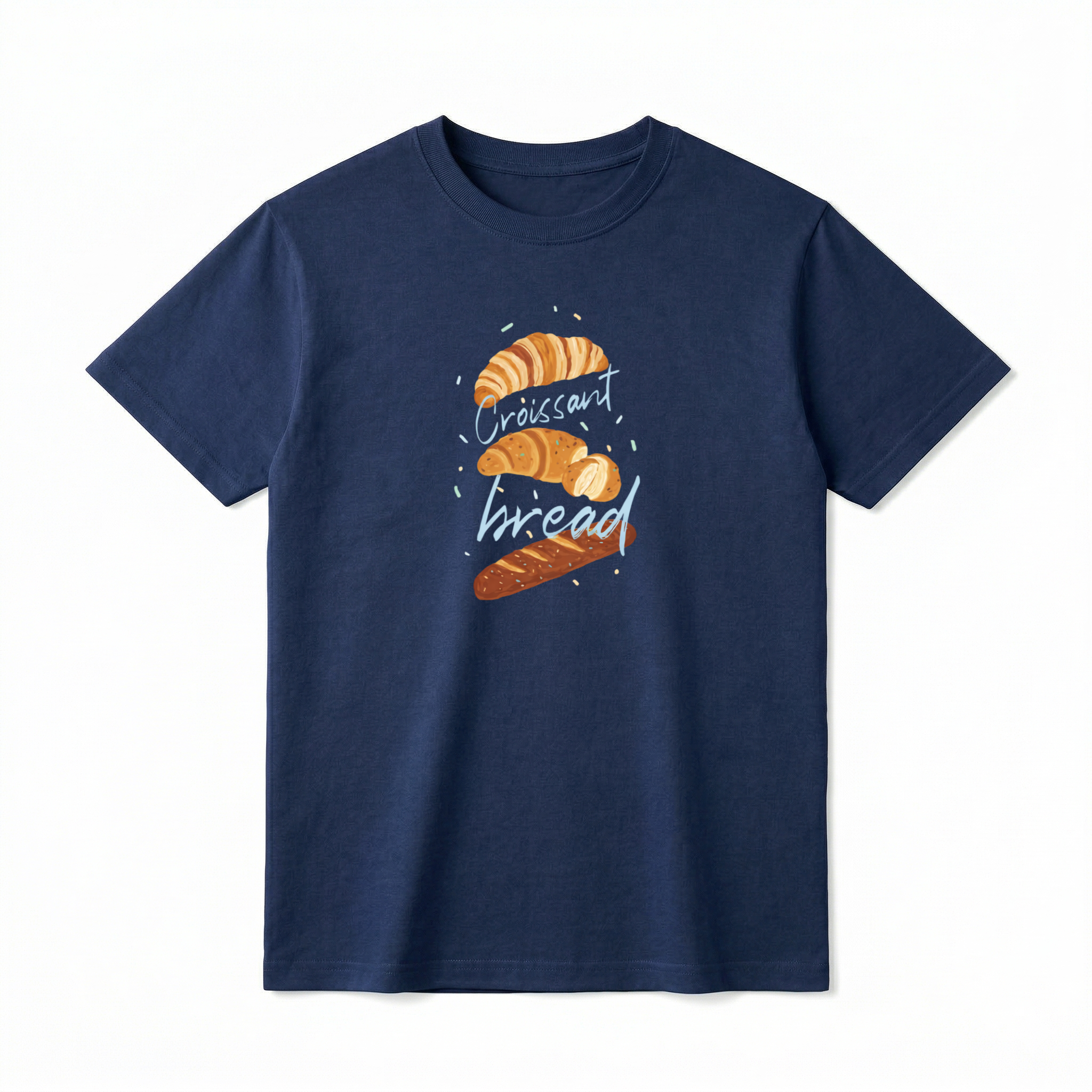 A flat lay of a short-sleeve t-shirt. The center chest features a hand-drawn graphic of vertically stacked baked goods: a golden croissant at the top, a sliced pastry in the middle, and a seeded baguette at the bottom. Light blue script text reading "Croissant" and "bread" is woven playfully across and between the pastries, surrounded by tiny, colorful confetti accents.